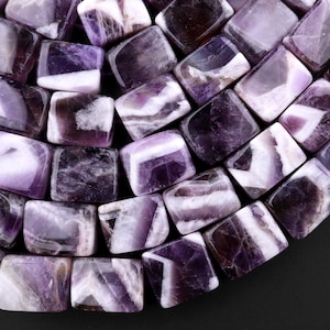 Puede incluir: Primer plano de una hebra de cuentas de piedra preciosa de amatista púrpura y blanca. Las cuentas son facetadas y tienen un acabado liso y pulido. Las cuentas están dispuestas en un patrón de semicírculo.