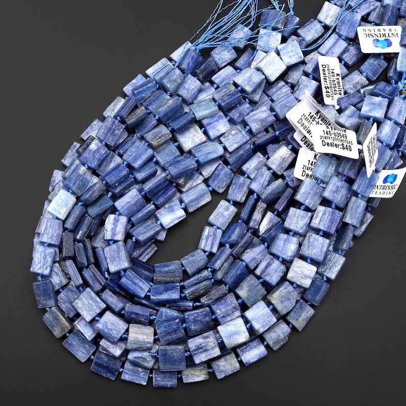 Puede incluir: Collar de cuentas de kianita azul. Las cuentas son rectangulares y est&aacute;n ensartadas en un cord&oacute;n azul. La kianita tiene diferentes tonos de azul. Se ven etiquetas con texto.