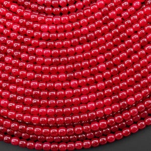 May include: Close-up of a collection of small, round, glossy red beads. The beads are arranged in a curved pattern, creating a textured surface. The beads are uniform in size and shape, reflecting light.