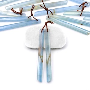 Puede incluir: Dos piedras largas, delgadas y de color azul claro aguamarina con lazos de cuerda marrón. Las piedras están sobre una superficie blanca.