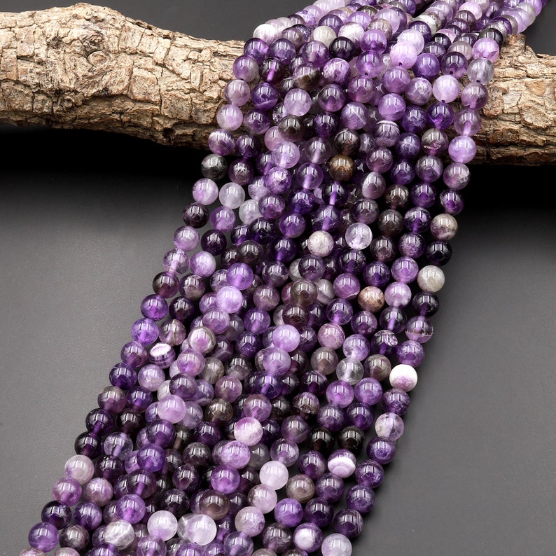 May include: A strand of round, purple amethyst beads. The beads are smooth and have a slight shimmer. The beads are strung on a clear thread.