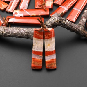 May include: A pair of red and white striped stone earrings. The earrings are rectangular in shape and have a polished finish.