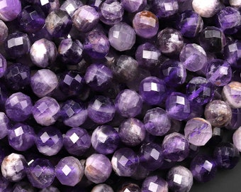 Könnte beinhalten: Nahaufnahme von facettierten Amethyst-Edelsteinperlen. Die Perlen zeigen eine Mischung aus tiefvioletten und helleren Lavendeltönen mit einer glänzenden, polierten Oberfläche. Die runden Perlen sind dicht gepackt und zeigen ihre geometrischen Facetten und natürlichen Farbvariationen.