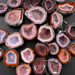 May include: A collection of pink and brown agate geode slices with a variety of shapes and sizes. The geode slices are arranged in a random pattern on a black surface.
