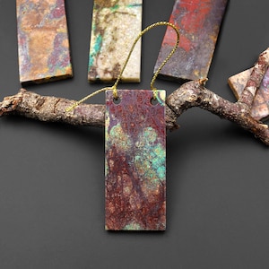 May include: Rectangular ornaments with a marbled appearance in shades of burgundy, teal, and gold. Each ornament has a gold string for hanging. The ornaments are displayed on a dark background with a tree branch.