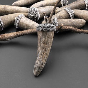 May include: A brown antler pendant with a silver setting and a black rhinestone embellishment. The antler is smooth and polished, and the setting is intricate and detailed.