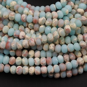 May include: Strands of gemstone beads in shades of pale blue, cream, and reddish-brown. The beads are oval-shaped and have a matte finish. The beads are strung together, creating a textured and colorful display. Ideal for jewelry making.