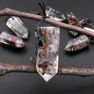 May include: A collection of six clear quartz crystal points with inclusions of green, black, and red. The crystals are arranged on a branch and have a natural, raw look.