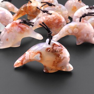 May include: A group of agate dolphin pendants with brown cords. The dolphins are carved from white agate with brown and pink inclusions.