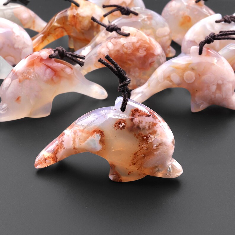 May include: A group of agate dolphin pendants with brown cords. The dolphins are carved from white agate with brown and pink inclusions.