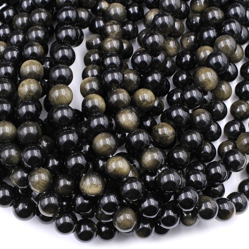 May include: A strand of black and gold gemstone beads. The beads are round and have a smooth, polished finish. The gold flecks in the beads are visible and add a touch of sparkle.