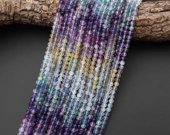 May include: A collection of multi-colored faceted gemstone beads arranged in long, vertical strands. The beads display a gradient of translucent hues including deep purple, soft lavender, pale yellow, and light blue, reflecting light across their surfaces.