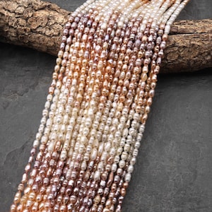 May include: A collection of multiple strands of small, irregular freshwater pearls in a gradient of colors ranging from white and cream to soft pink, peach, and light purple, arranged in parallel vertical lines with a lustrous finish.