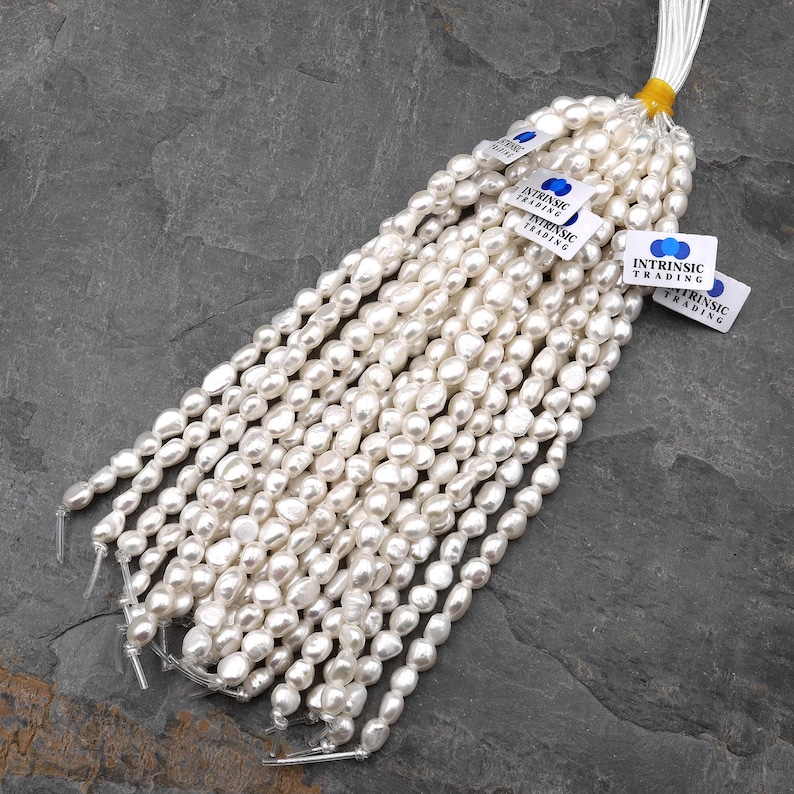 Puede incluir: Hilos de perlas blancas de forma irregular, probablemente de agua dulce, est&aacute;n agrupados. Cada hilo est&aacute; ensartado con un hilo visible. Peque&ntilde;as etiquetas blancas con el texto "INTRINSIC TRADING" est&aacute;n adjuntas.
