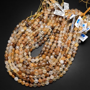 May include: A strand of golden quartz beads, approximately 8mm in size, with a faceted finish. The beads are a mix of light and dark golden hues, with some having a smoky or cloudy appearance. The beads are strung on a yellow thread and are ready for jewelry making.
