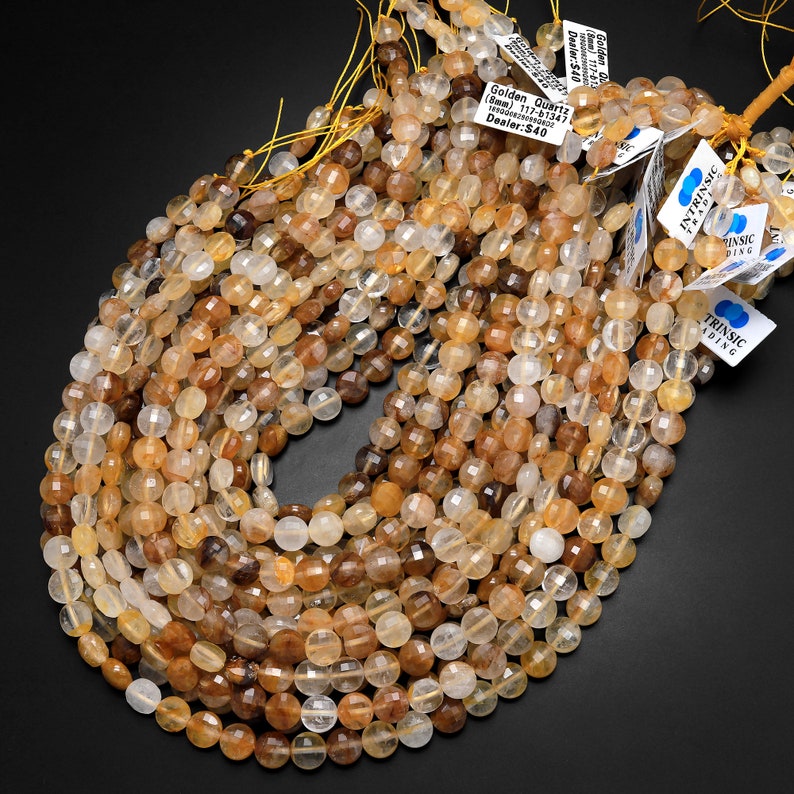 May include: A strand of golden quartz beads, approximately 8mm in size, with a faceted finish. The beads are a mix of light and dark golden hues, with some having a smoky or cloudy appearance. The beads are strung on a yellow thread and are ready for jewelry making.