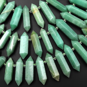 May include: A collection of green gemstone beads in a faceted, pointed shape. The beads are strung on clear elastic cord.