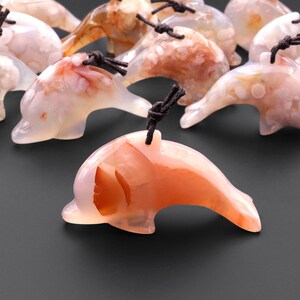 May include: A collection of carved agate dolphin pendants with brown cords. The dolphins are carved in a variety of shades of pink, white, and brown agate.