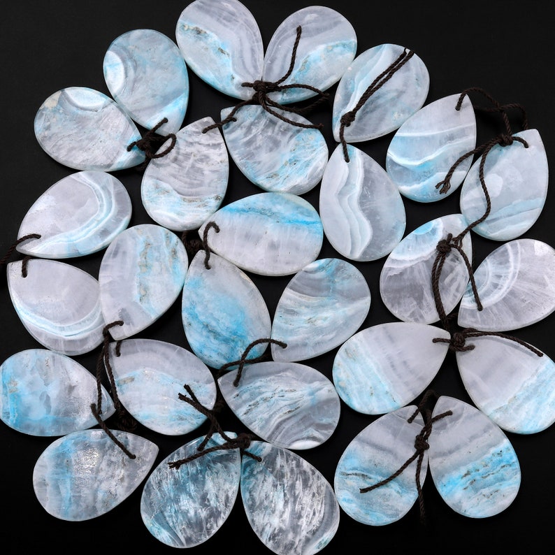 May include: A collection of 20 teardrop-shaped pendants made of blue and white agate. Each pendant has a unique pattern of blue and white swirls and is strung with a brown cord.