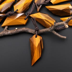 May include: A collection of gold tiger's eye pendants with a geometric shape, each pendant is attached to a brown cord.