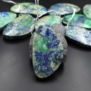 Puede incluir: Un colgante hecho de una piedra preciosa verde y azul con una cadena de plata. La piedra preciosa es una mezcla de colores verde, azul y blanco.