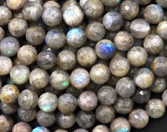 May include: A collection of round, faceted labradorite beads. The beads are primarily gray with iridescent flashes of blue, green, and gold. The beads are of varying sizes and are tightly packed together.