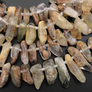 Op de afbeelding: Een streng lichtgroene, bruine en heldere kwartskristal kralen. De kralen zijn onregelmatig van vorm en hebben een ruwe, natuurlijke textuur.