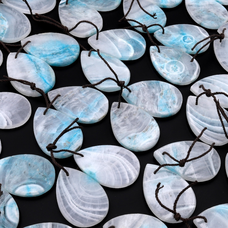 May include: A collection of teardrop-shaped pendants made of white and blue agate with brown string attached to each pendant.