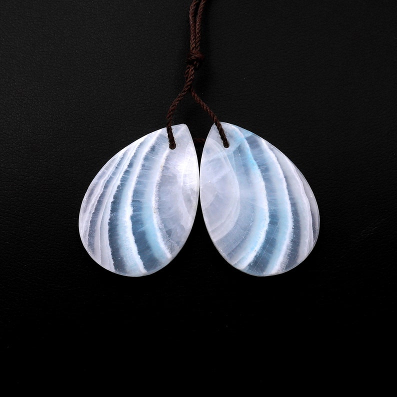May include: A pair of teardrop-shaped blue and white gemstone pendants with a brown cord.