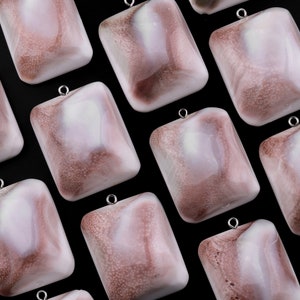 Può includere: Una collezione di ciondoli quadrati con un design marmoreo bianco e marrone. I ciondoli hanno una finitura lucida e sono infilati su catene d'argento.