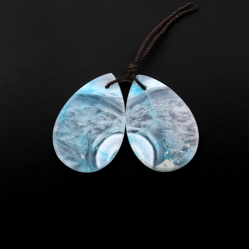 May include: A pair of teardrop-shaped blue and white gemstone pendants with a brown cord.