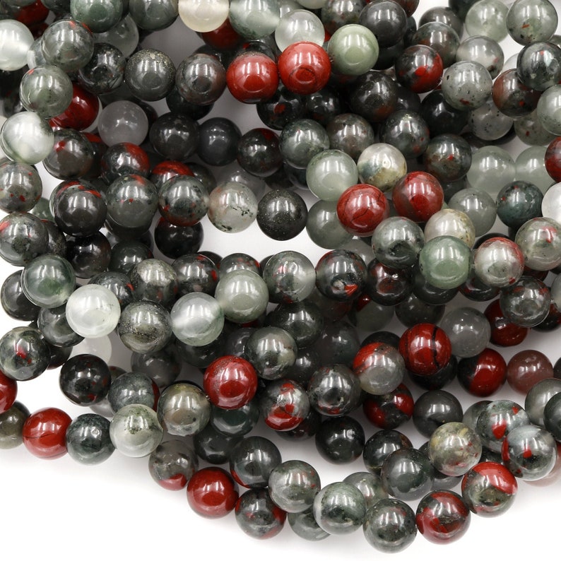 May include: A strand of round, green and red gemstone beads. The beads are a mix of light and dark green with red speckles and solid red beads.