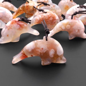 May include: A group of white and red agate dolphin pendants with brown cords. The dolphins have a white and red agate pattern with white spots.