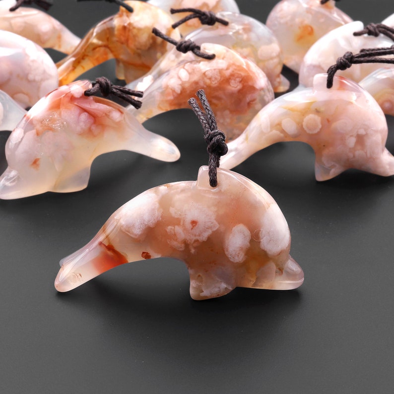 May include: A group of white and red agate dolphin pendants with brown cords. The dolphins have a white and red agate pattern with white spots.