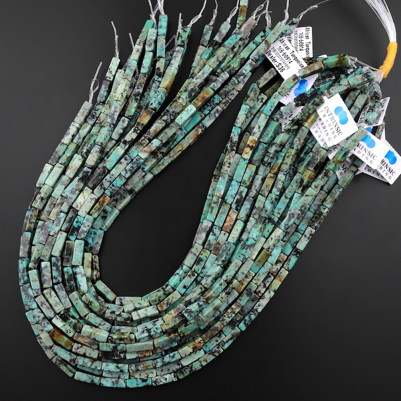 May include: A strand of turquoise beads, each bead is a rectangular shape with a mottled green and brown pattern. The beads are strung on a clear thread and are ready to be used for jewellery making.