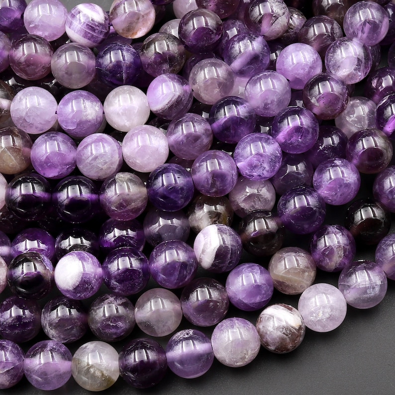 May include: A strand of round, purple amethyst beads. The beads have a smooth, polished finish and a variety of shades of purple, from light lavender to deep violet.