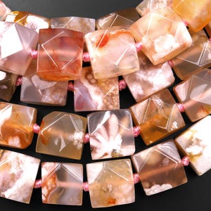 Può includere: Primo piano di una collana con perline di agata traslucide a taglio quadrato nei toni dell'arancione, pesca e bianco. Le perline sono infilate con un cordoncino rosa, creando un motivo geometrico. Le perline di agata hanno motivi interni unici.