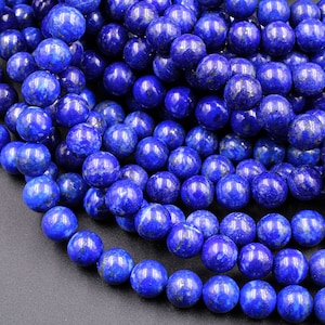 Puede incluir: Una hebra de cuentas de lapisl&aacute;zuli azul oscuro con motas de pirita dorada. Las cuentas son redondas y lisas, y est&aacute;n dispuestas en un mont&oacute;n suelto.