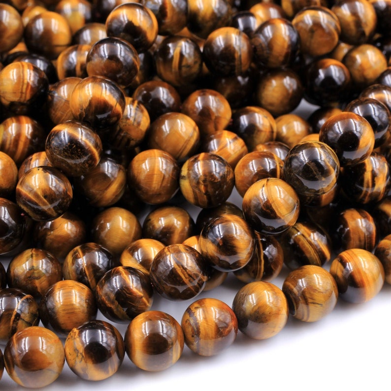 May include: A strand of round, polished tiger's eye beads in shades of brown and gold. The beads are smooth and have a slight sheen.