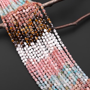 May include: Strands of square gemstone beads in various colors, including pink, white, brown, and blue. The beads are strung together with silver-colored spacers. The beads are arranged in a cascading pattern, with a dark background.