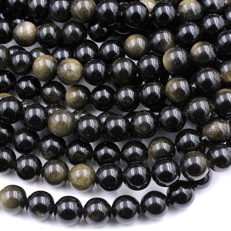 May include: A strand of black and gold gemstone beads. The beads are round and have a smooth, polished finish.