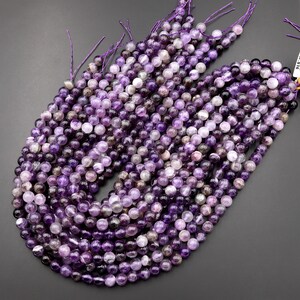 May include: A strand of amethyst beads, each bead is a round, smooth, and polished purple gemstone. The beads are strung on a thin, purple thread.