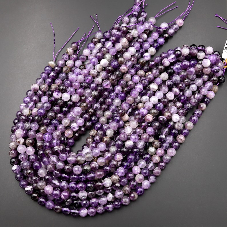 May include: A strand of amethyst beads, each bead is a round, smooth, and polished purple gemstone. The beads are strung on a thin, purple thread.