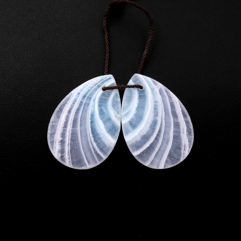 May include: A pair of light blue and white banded teardrop-shaped gemstone pendants with a brown cord.