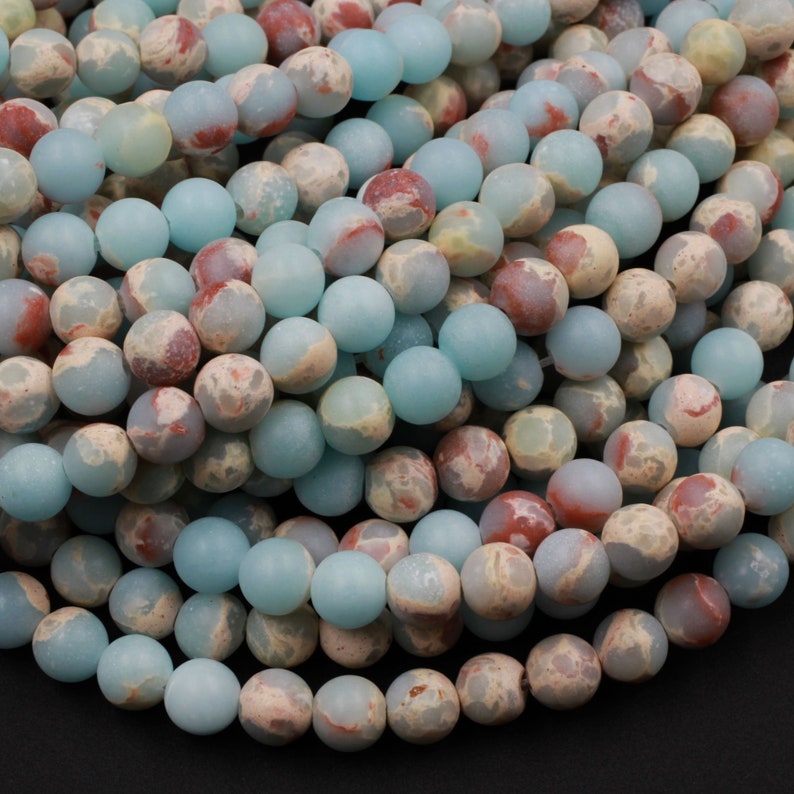 K&ouml;nnte beinhalten: Eine Str&auml;hne aus blauen, wei&szlig;en und roten Jaspisperlen. Die Perlen sind rund und haben eine matte Oberfl&auml;che.