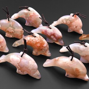 May include: A group of ten agate dolphin pendants with brown cords. The dolphins are carved from white agate with brown and pink markings.