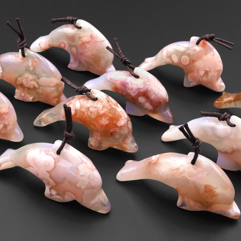 May include: A group of ten agate dolphin pendants with brown cords. The dolphins are carved from white agate with brown and pink markings.