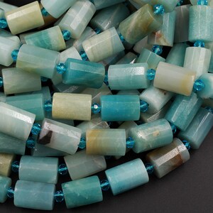 Pode incluir: Um fio de contas de pedra preciosa amazonita azul claro e verde com formato cil&iacute;ndrico facetado. As contas s&atilde;o enfiadas com contas facetadas de cor azul escuro menores.