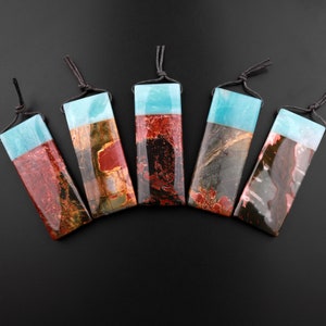 May include: Five rectangular pendants made of red, brown, and black jasper with a blue top. Each pendant has a black cord attached.