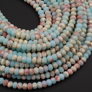 May include: Close-up of strands of gemstone beads. The beads are a mix of pale blue, cream, and reddish-brown colors. The beads are round with a slightly flattened shape. The background is black.